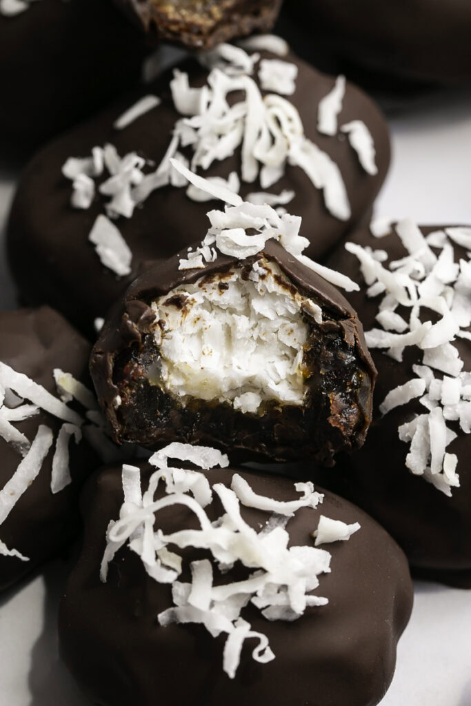 close up of Vegan Bounty Bar Coconut Stuffed Dates in a pile, one with a bite taken out of it to reveal the coconut filling.
