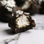 close up of Vegan Bounty Bar Coconut Stuffed Date with a bite taken out of it to reveal the coconut filling.
