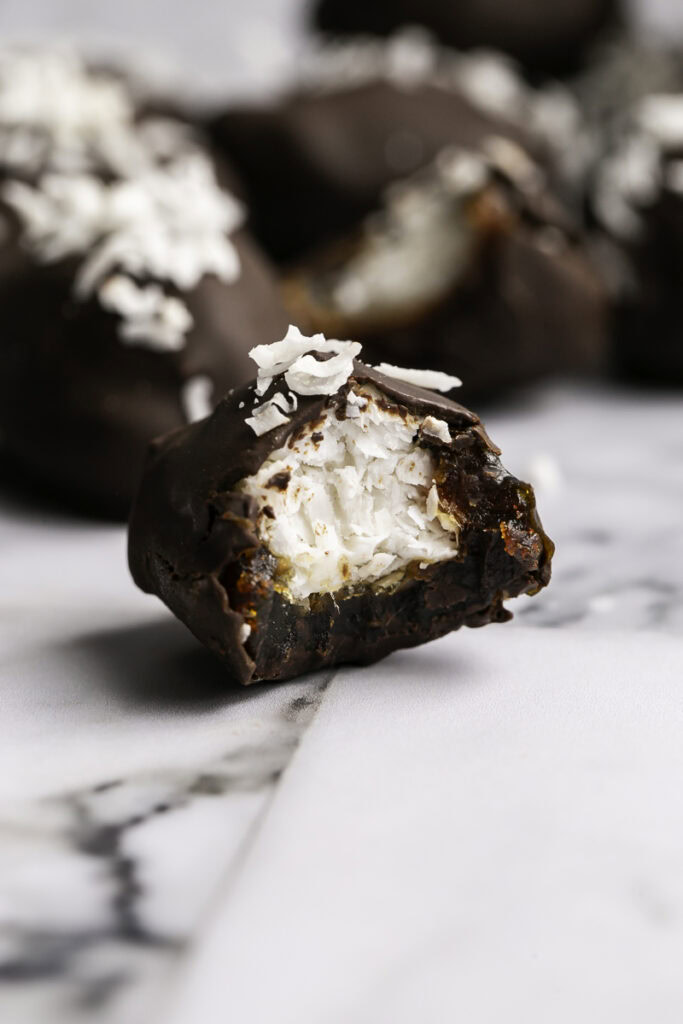 close up of Vegan Bounty Bar Coconut Stuffed Date with a bite taken out of it to reveal the coconut filling.