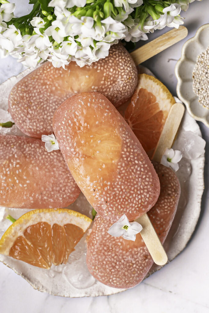 grapefruit chia seed popsicles on a plate with ice and fresh grapefruit slices.