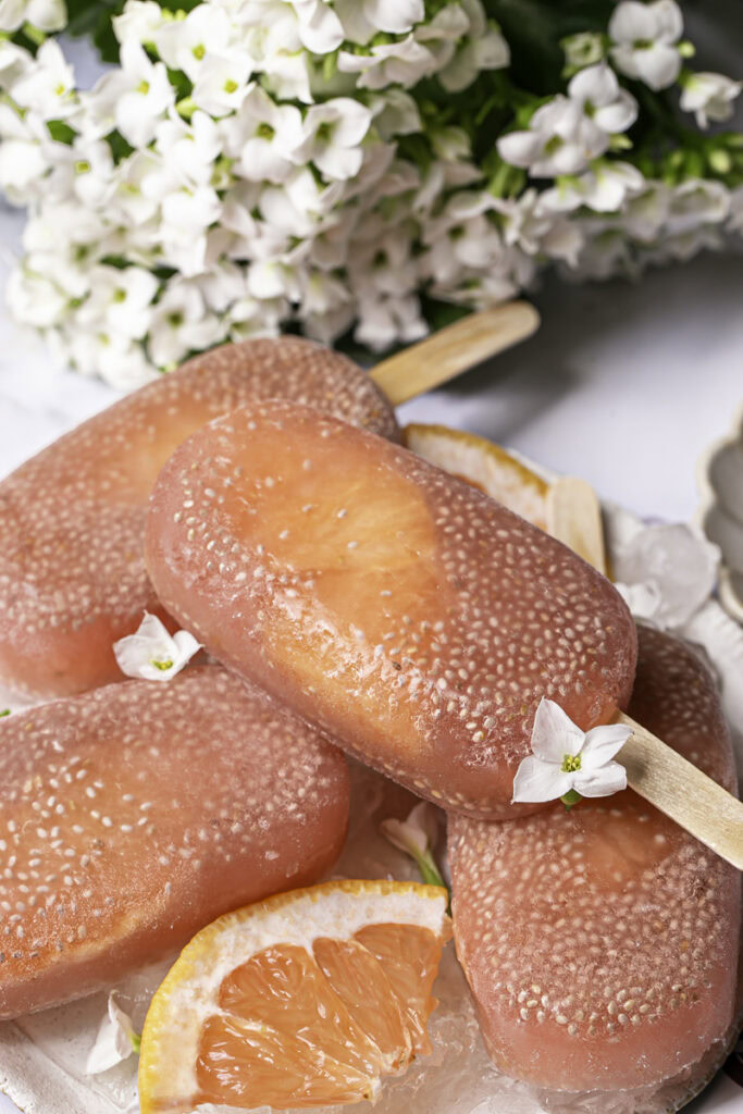 3/4 shot of grapefruit chia seed popsicles on a plate with ice and fresh grapefruit slices.