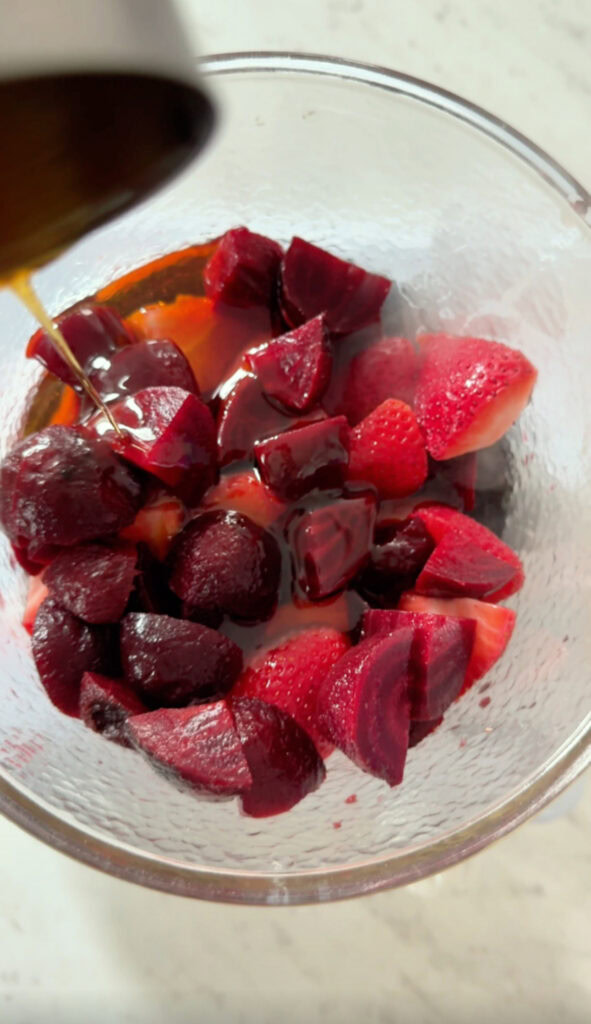 pouring maple syrup into the saucepan with strawberries and beets.