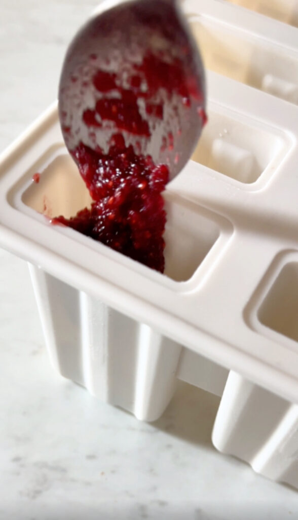 spooning strawberry beet chia seed jam into a popsicle mold.