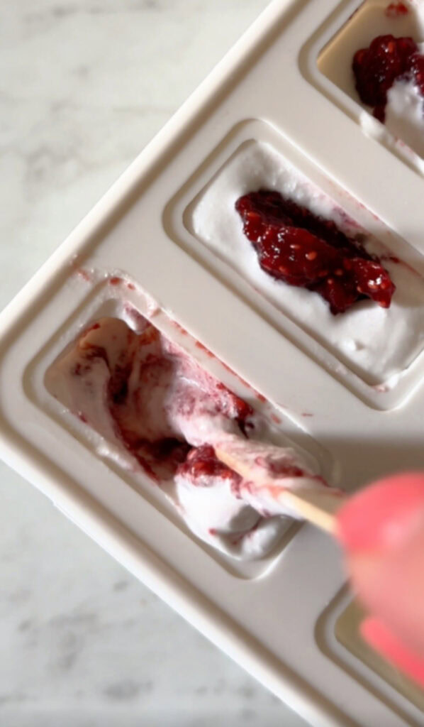 stirring the coconut milk and strawberry beet chia seed jam together with a popsicle stick in the popsicle mold.