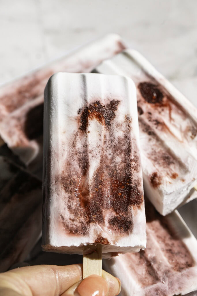 a hand holding a Strawberry Beet Chia Seed Jam Coconut Milk Popsicle.