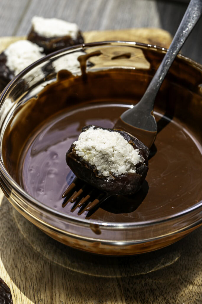 a fork dipping the coconut stuffed date into melted chocolate.