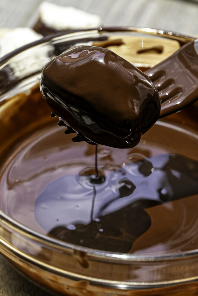 a fork raising a coconut stuffed date out of the melted chocolate completely coated in melted chocolate.
