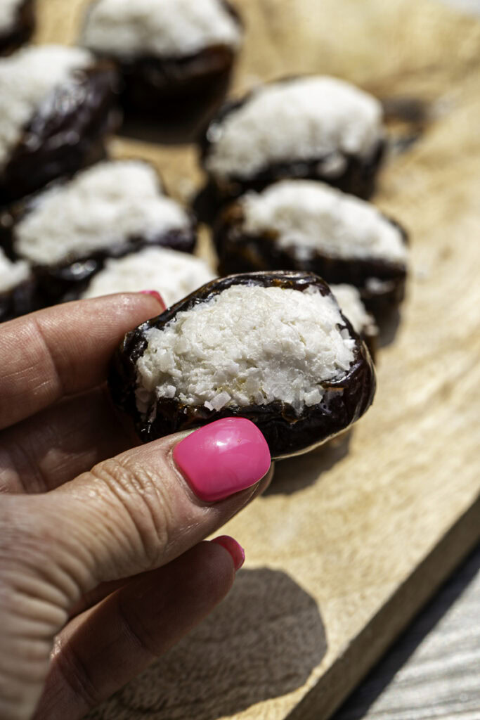 a hand holding a date stuffed with coconut filling.