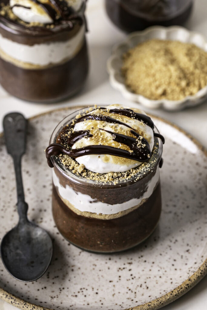 3/4 shot of chocolate S'mores Chia Pudding in jars on a plate with a spoon.