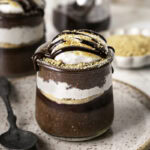 chocolate S'mores Chia Pudding in jars on a plate with a spoon.