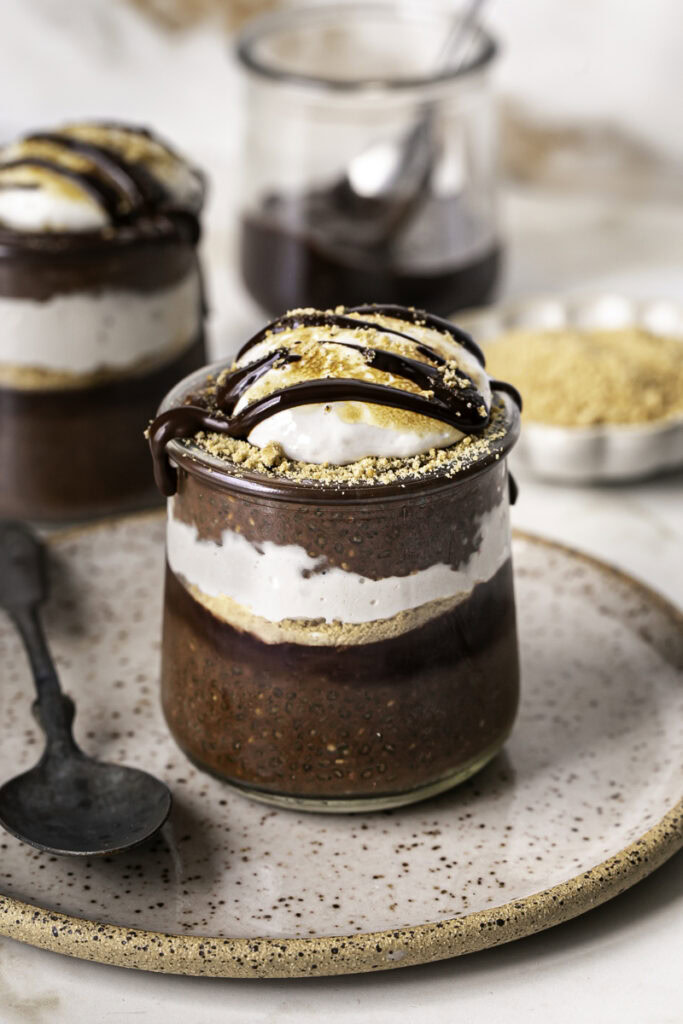 chocolate S'mores Chia Pudding in jars on a plate with a spoon.