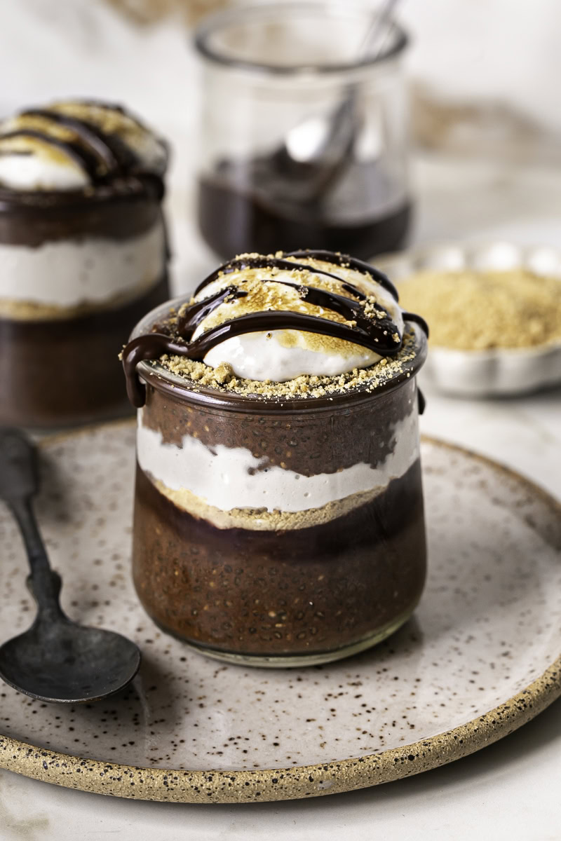 chocolate S'mores Chia Pudding in jars on a plate with a spoon.