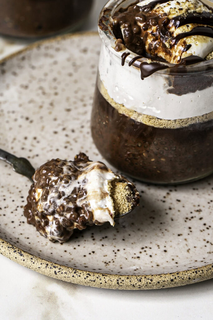 close up of chocolate s'mores chia pudding in a jar with a scoop on the spoon resting on a plate.