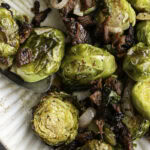 close up of maple bacon brussels sprouts on an oval serving plate with a serving spoon.