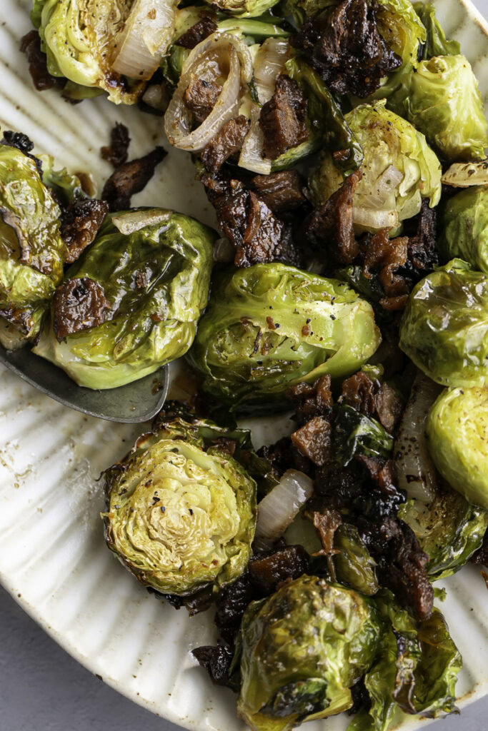 close up of maple bacon brussels sprouts on an oval serving plate with a serving spoon.