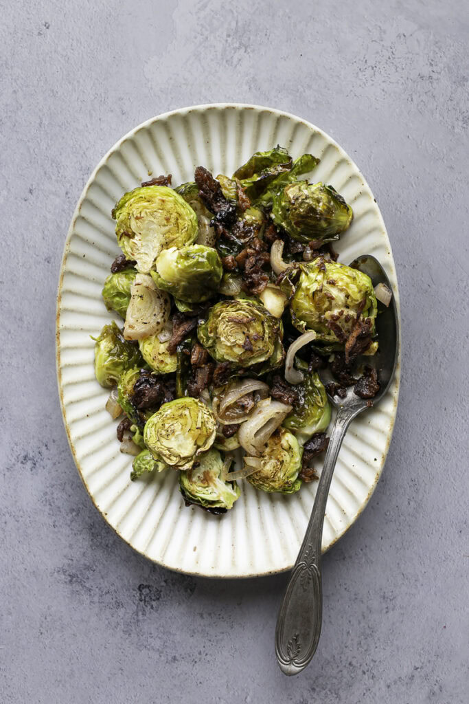 maple bacon brussels sprouts on an oval serving plate with a serving spoon.