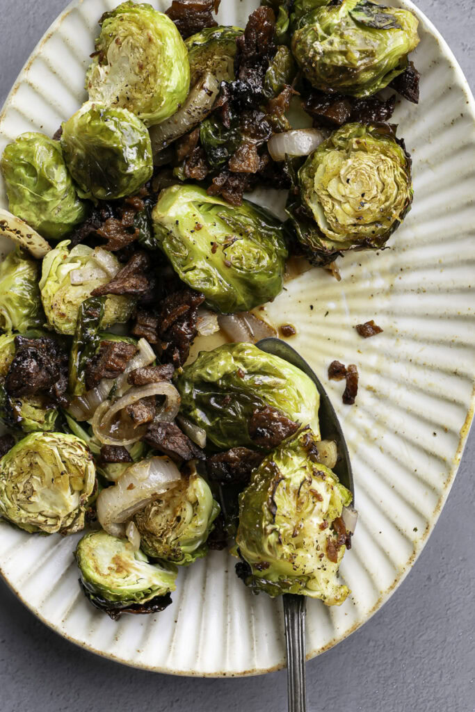maple bacon brussels sprouts on an oval serving plate with a serving spoon.