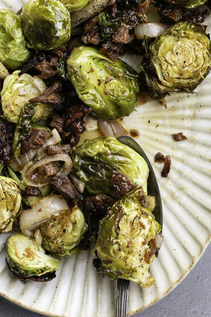 maple bacon brussels sprouts on an oval serving plate with a serving spoon.