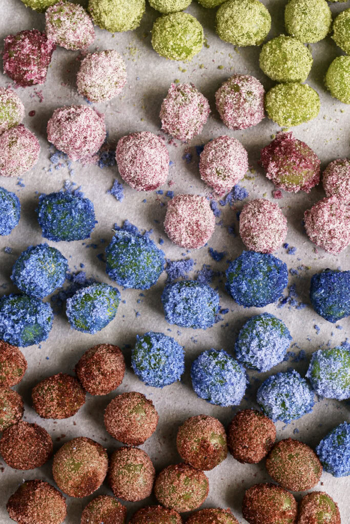 all of the rolled colored grapes on a parchment-lined baking sheet ready to be frozen.