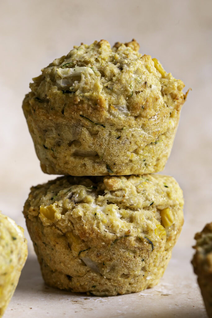 two zucchini cornbread muffins stacked on top of one another.