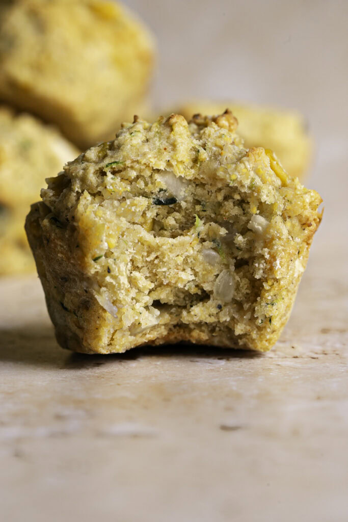 a single zucchini cornbread muffin with a bite taken out of it to reveal the muffin texture.