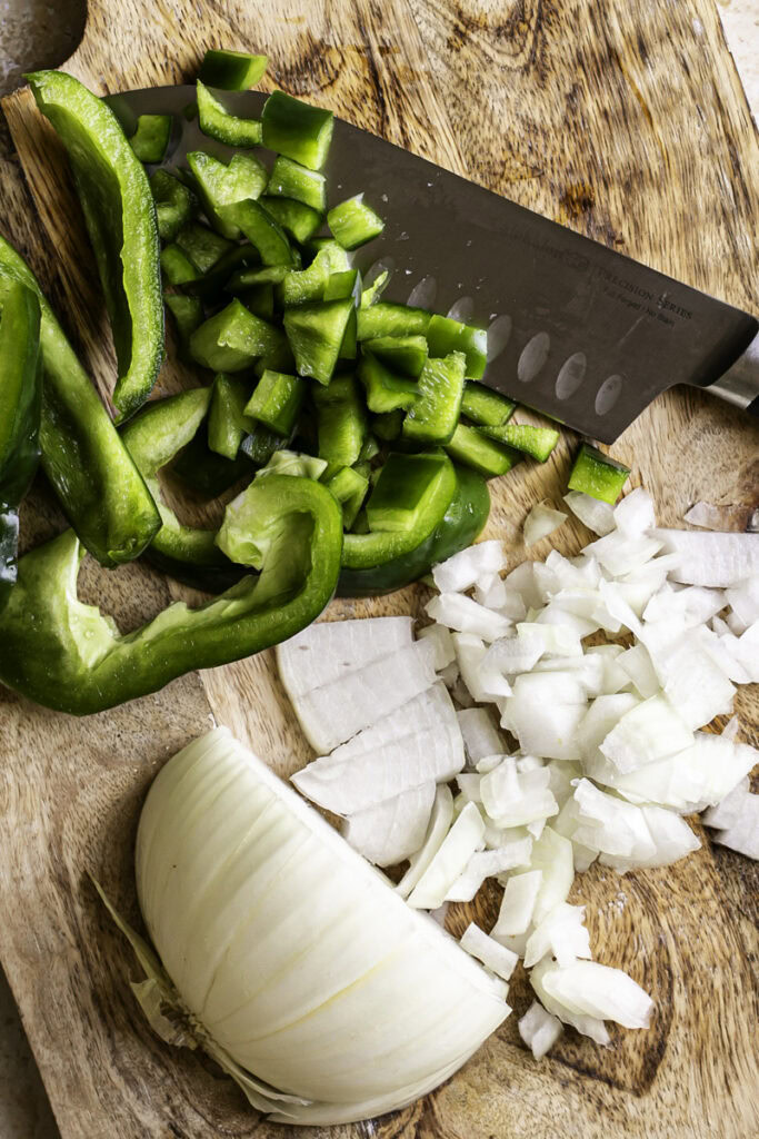 diced green pepper and onion on a wooden cutting board with a knife.