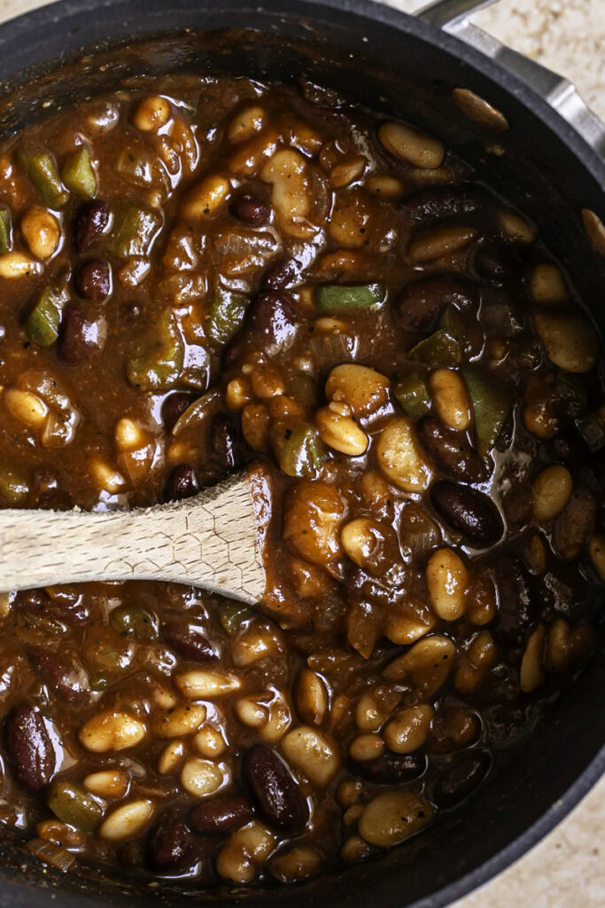 3 Bean Stovetop Baked Beans cooking in a saucepan with a wooden spoon in the pot.