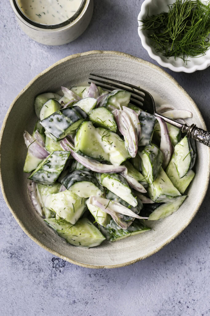 overhead shot of easy dairy-free creamy cucumber salad with a jar of dressing and a bowl of fresh dill.