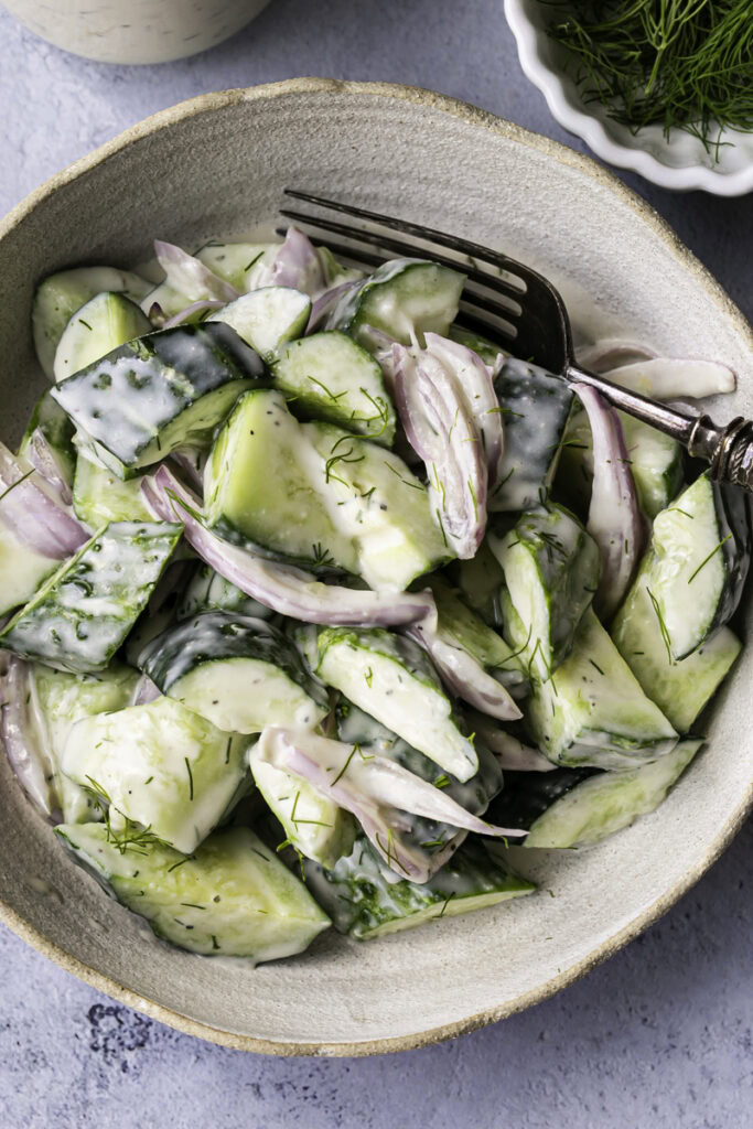 close up overhead shot of easy dairy-free creamy cucumber salad with a jar of dressing and a bowl of fresh dill.