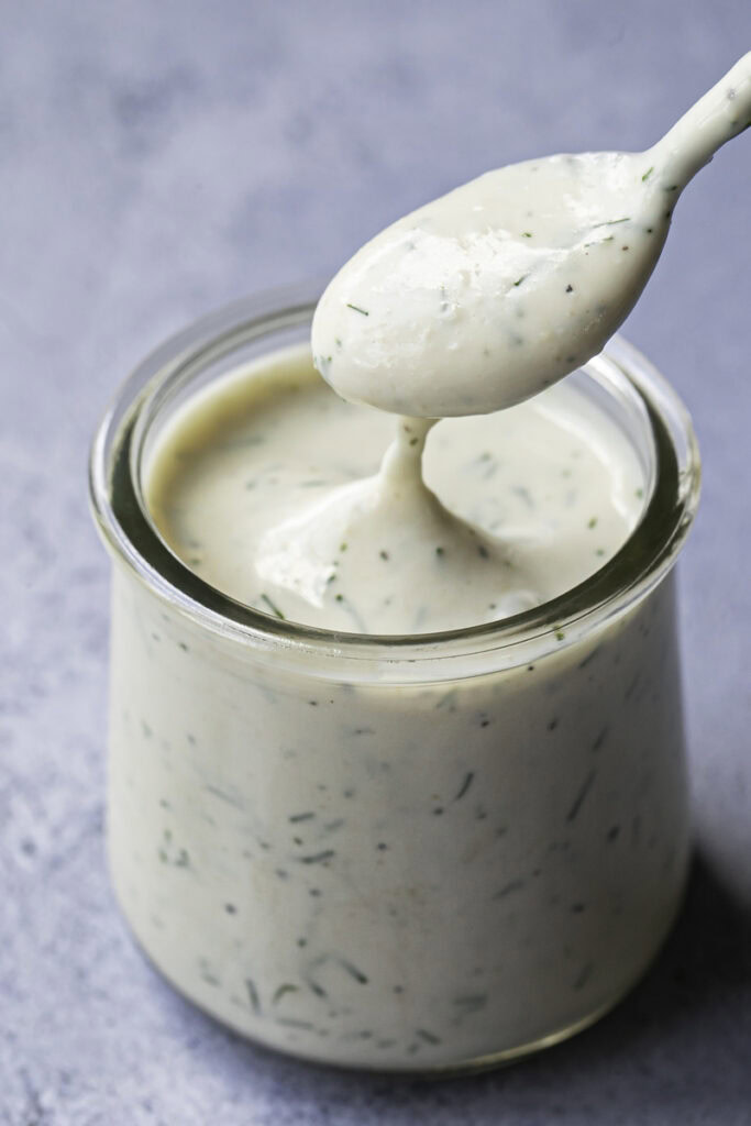 a jar of creamy dill yogurt sour cream dressing with a spoon dripping some back into the jar.