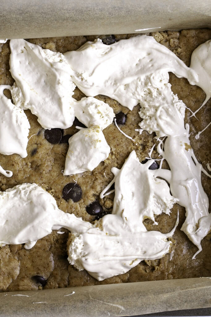 marshmallow fluff dolloped on top of half of the cookie dough pressed into a square baking pan.