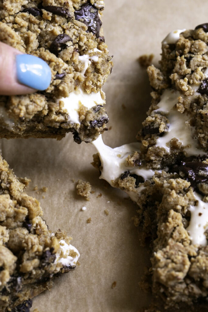 action shot of a hand pulling away a smores cookie crumb bar with a string of melty marshmallow fluff.