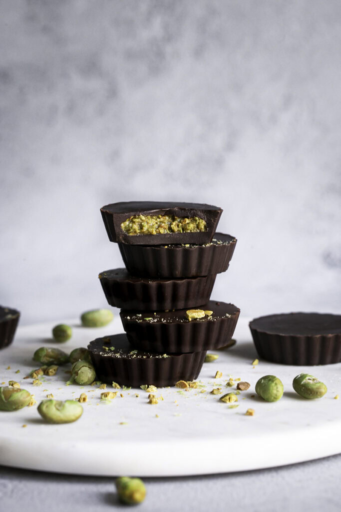 crunchy chocolate edamame butter cups stacked on top of one another, the top one with a bite taken out of it.