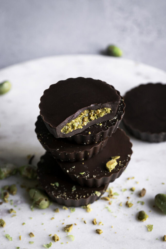 3/4 shot of crunchy chocolate edamame butter cups stacked on top of one another, the top one with a bite taken out of it.