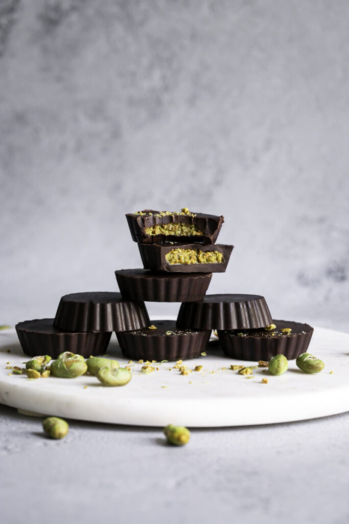 crunchy chocolate edamame butter cups stacked on top of one another in a pyramid style shape, the top two with a bite taken out of them.