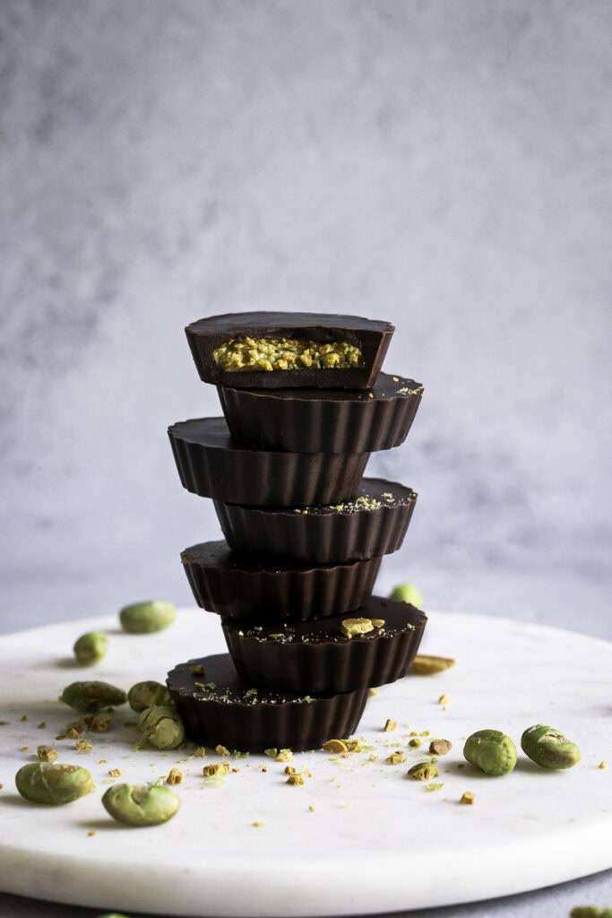 crunchy chocolate edamame butter cups stacked on top of one another, the top one with a bite taken out of it.