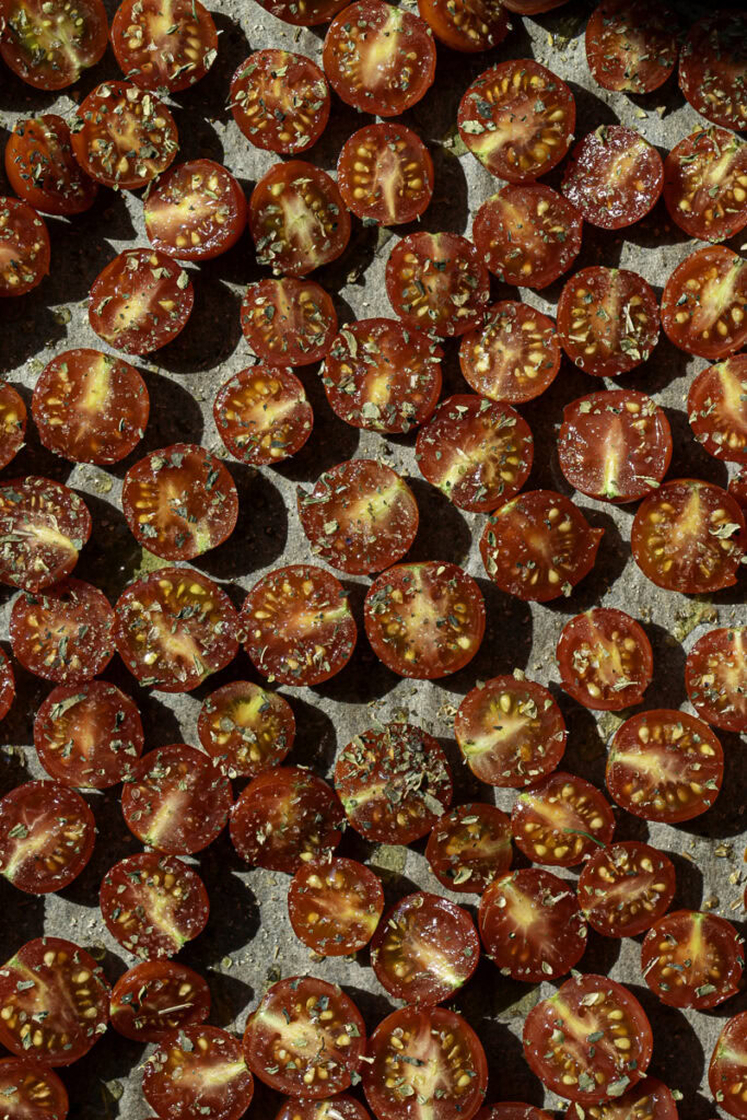 sliced cherry tomatoes on a parchment lined baking sheet drizzled with olive oil, sprinkled with salt and dried herbs.