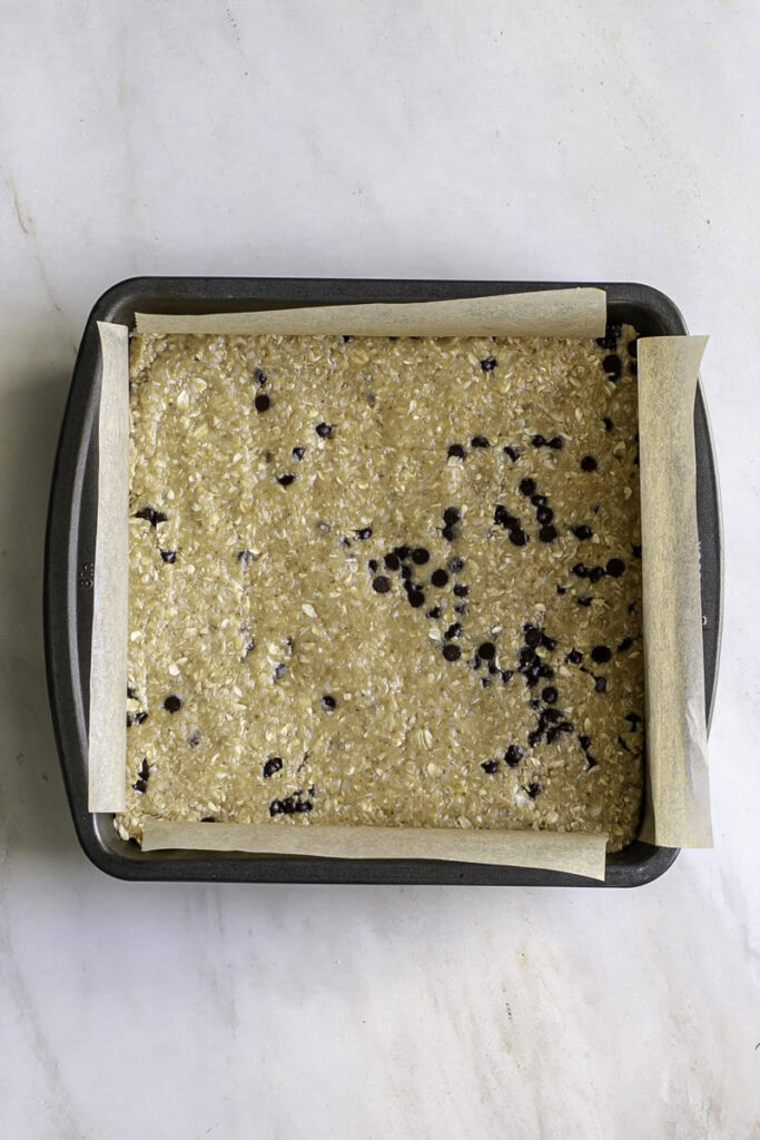 cookie dough pressed into an 8x8 parchment-lined baking pan.