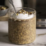 pumpkin spice espresso overnight oats in a glass with a spoon topped with coconut cream, and chopped nuts.