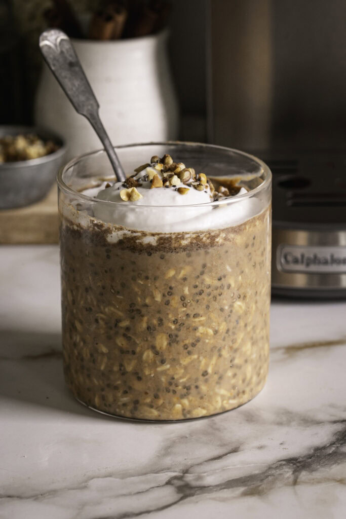 pumpkin spice espresso overnight oats in a glass with a spoon topped with coconut cream, and chopped nuts.