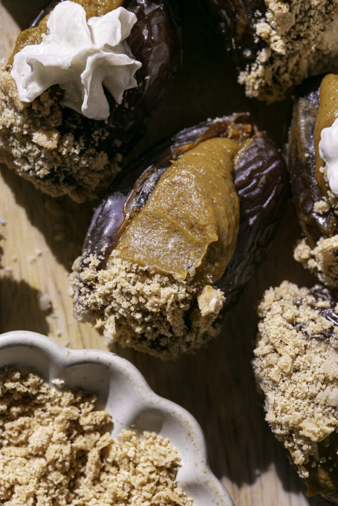 pumpkin pie stuffed dates on a wooden cutting board with a bowl of crushed graham cracker crumbs.