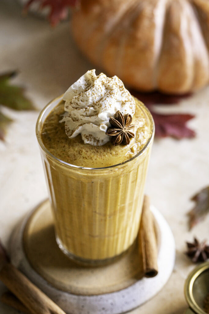 pumpkin pie smoothie in a glass with pumpkins and leaves in the background.
