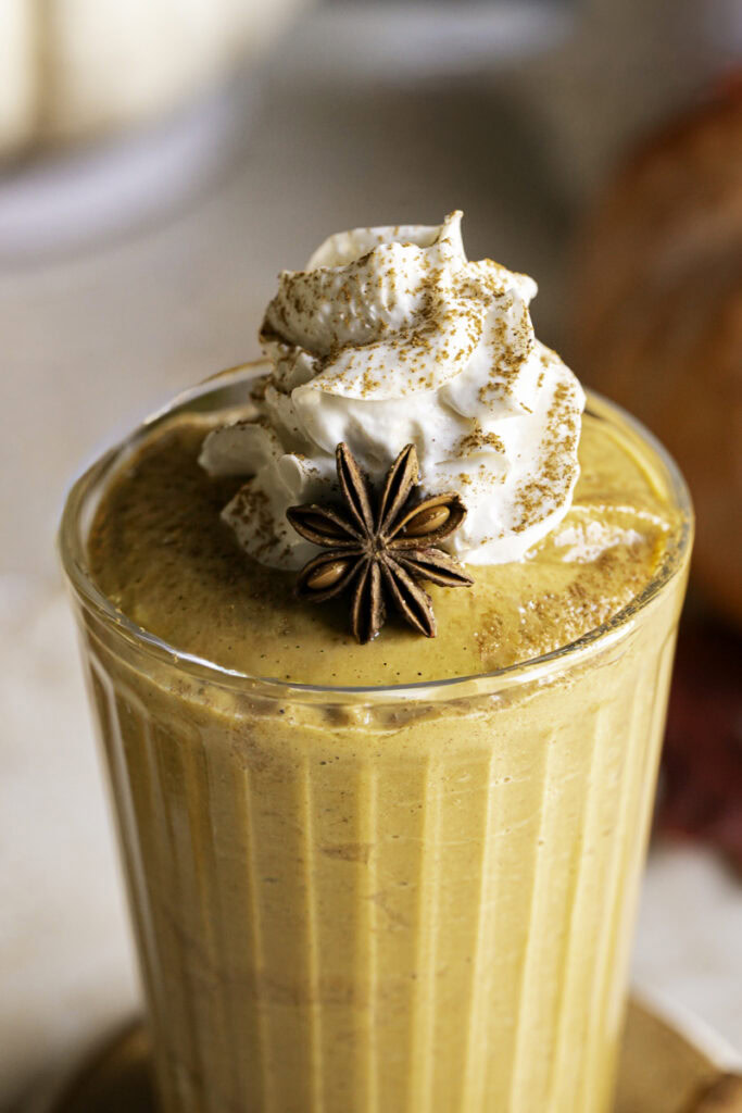 close up of the top half of a pumpkin pie smoothie in a glass with whipped cream and sprinkled cinnamon on top.