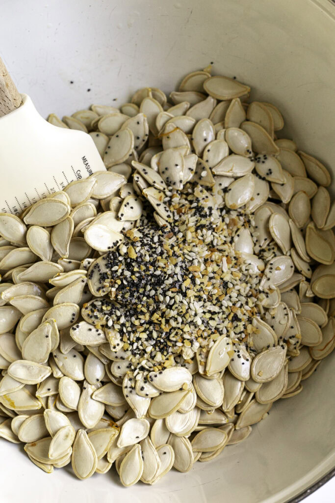 raw pumpkin seeds in a bowl with everything bagel seasoning and a spatula.