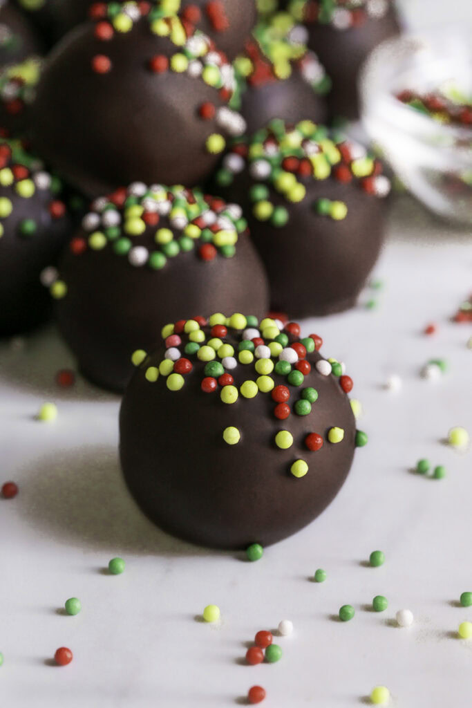 close up 3/4 image of No-Bake Chocolate Gingerbread Almond Flour Cookie Dough Bites decorated with red and green sprinkles.