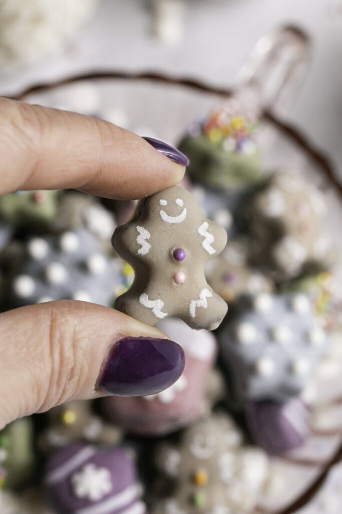 fingers holding a mini gingerbread man cookie with the rest of the cookies blurred in the background.