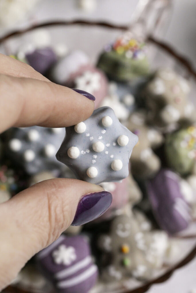 fingers holding a mini snowflake cookie with the rest of the cookies blurred in the background.
