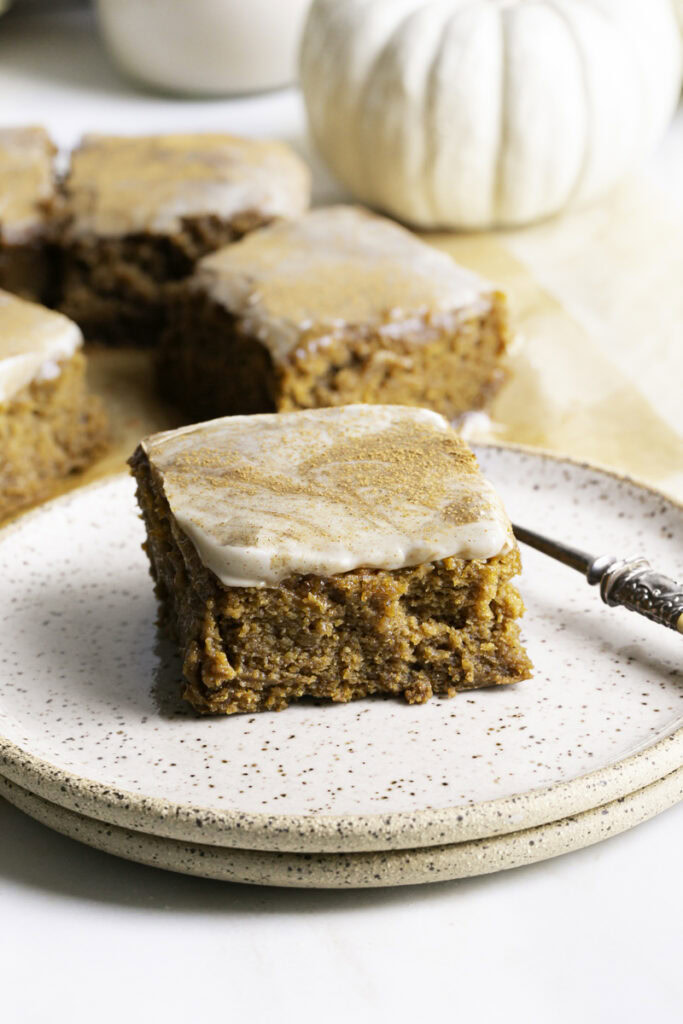 pumpkin olive oil cake on a stack of two plates with a fork, more pumpkin cake slices in the background.