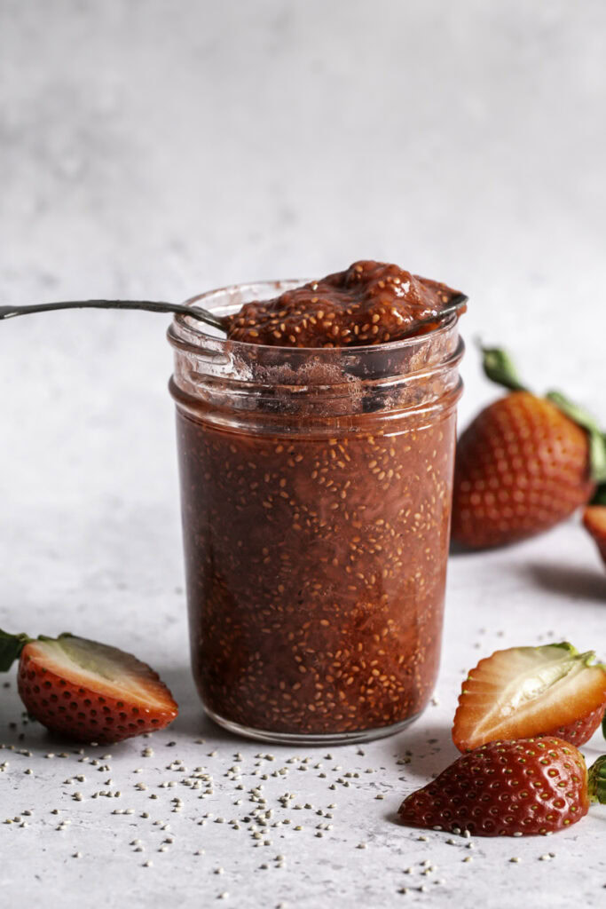a spoonful of strawberry chia seed jam resting on top of the jar of jam with fresh strawberries around it.