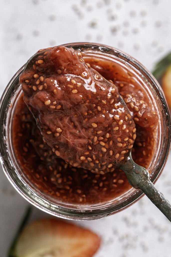 closeup overhead shot of strawberry chia seed jam on a spoon resting on the jar of jam.